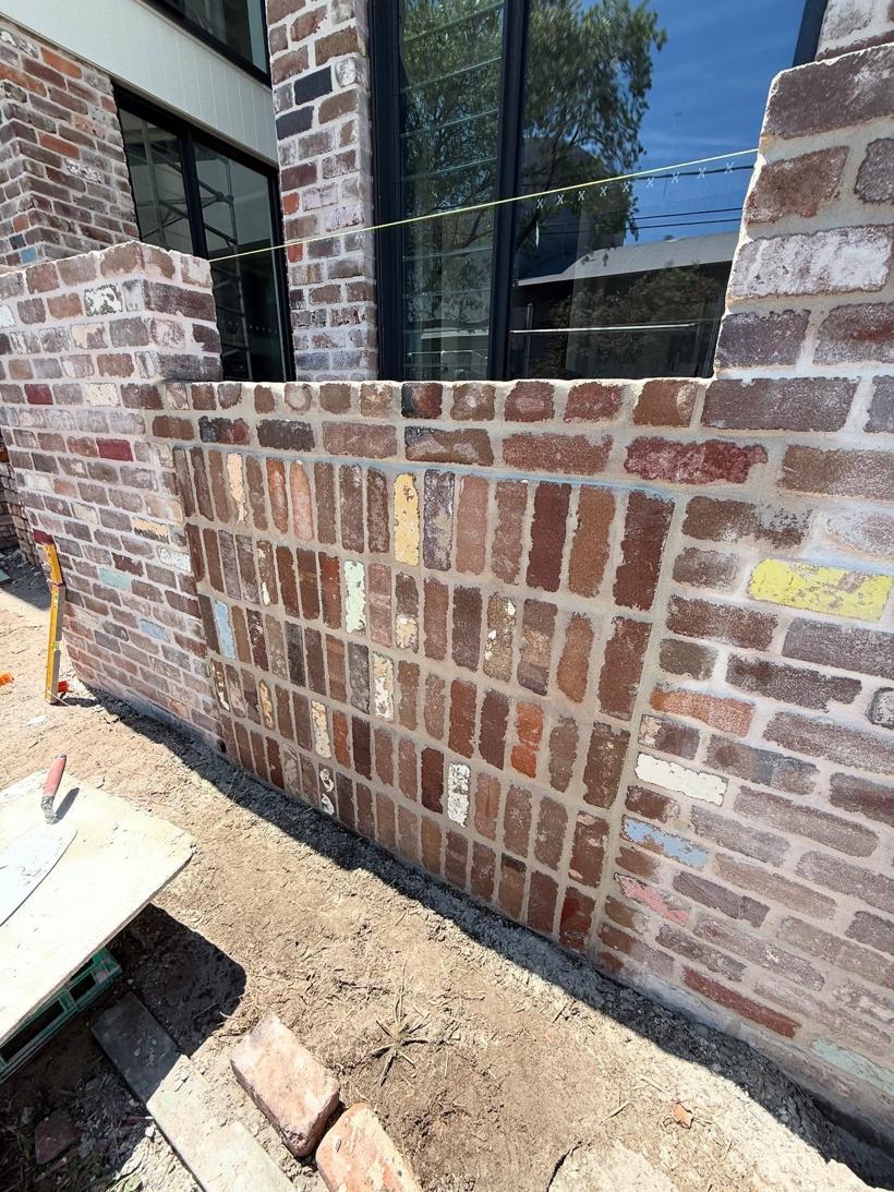 Recycled-brick fence with soldier-course capping along a new home